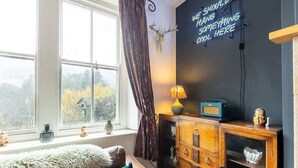 A cozy room with a large window, a fur throw on the sofa, a vintage radio, and a wall sign. - Three Bed Cottage in the heart of the Peaks (Edale)