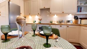 A kitchen with white cabinets, a green polka dot tablecloth, and a wine glass on the table. - Three Bed Cottage in the heart of the Peaks (Edale)