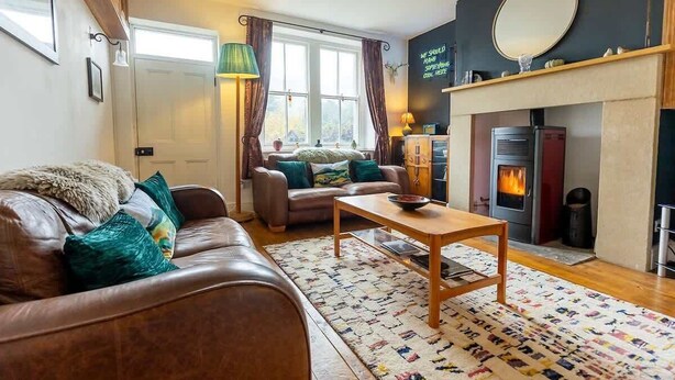 A cozy living room with a fireplace, leather sofa, and a coffee table. - Three Bed Cottage in the heart of the Peaks (Edale)