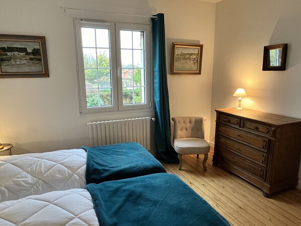 Un dormitorio con dos camas, un tocador, una silla y una ventana con cortinas.