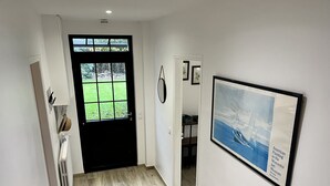 Un couloir avec un plancher en bois, une porte noire et un tableau encadré représentant un navire, accroché au mur.