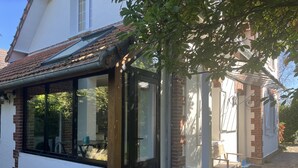 Une maison dotée d’un patio couvert, d’une cheminée en briques et d’un petit espace extérieur aménagé pour s’asseoir.