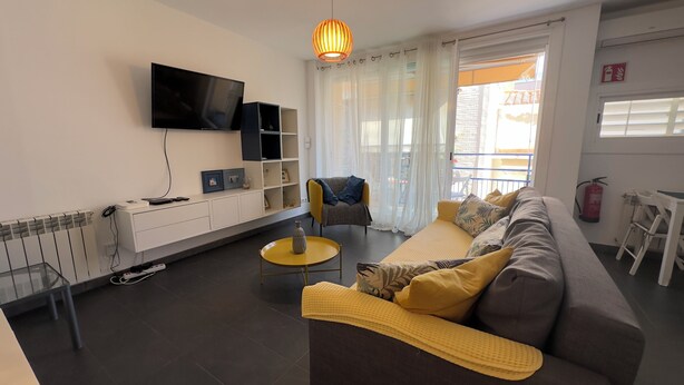 Un soggiorno moderno con divano, tavolino, televisore a parete e un balcone con vista.