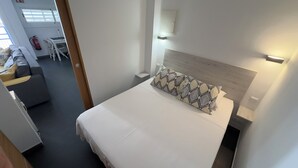 Una camera d'albergo con un letto, un comodino, una lampada a parete e una finestra con persiane.