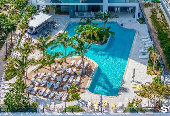An aerial view of a resort with a large pool, sun loungers, and palm trees.