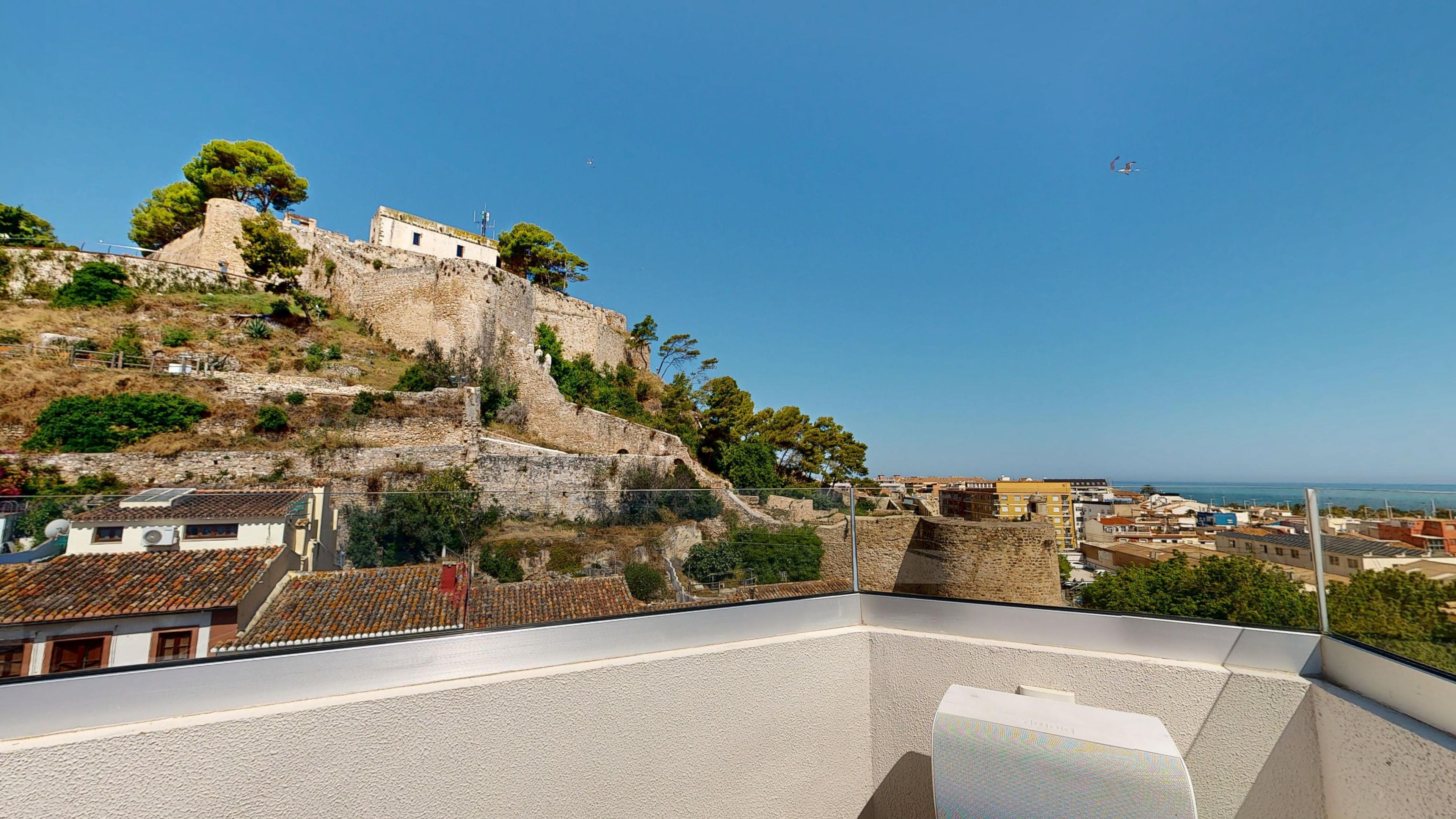 A view from a balcony overlooking a historic stone fortification with a clear sky and distant cityscape.