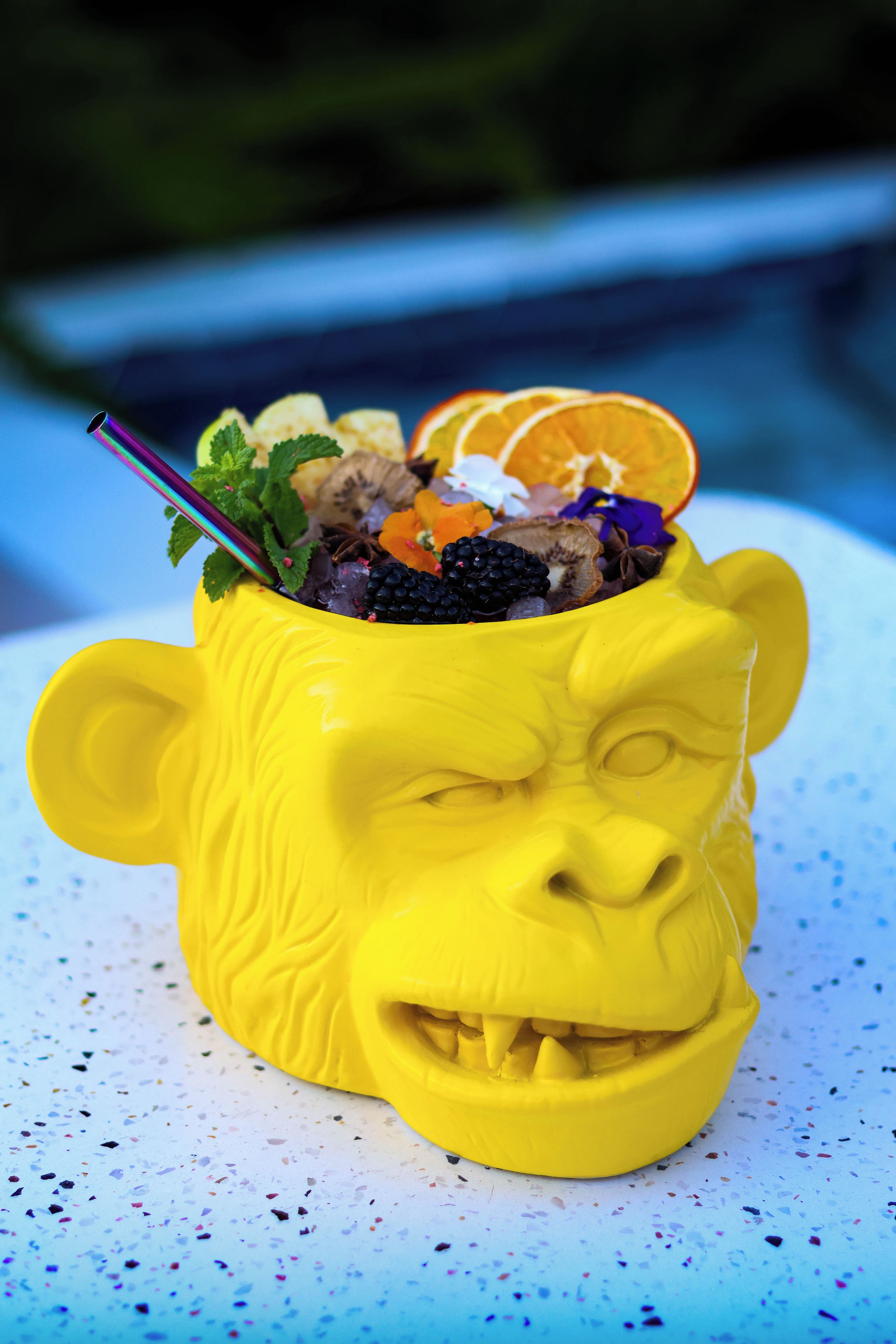 Una taza amarilla de cerámica con diseño de rostro, que contiene una mezcla de bebida colorida y adornos.