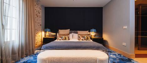 A bedroom with a large bed, bedside lamps, a bench, and a patterned carpet.