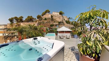 A rooftop terrace with a hot tub, outdoor seating, and a view of a historic hilltop structure.