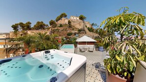 A rooftop terrace with a hot tub, outdoor seating, and a view of a historic hilltop structure. - Nomada House by SH Hoteles  (Denia)