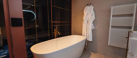 A modern bathroom with a freestanding bathtub, a glass-enclosed shower, and a towel rack with robes.