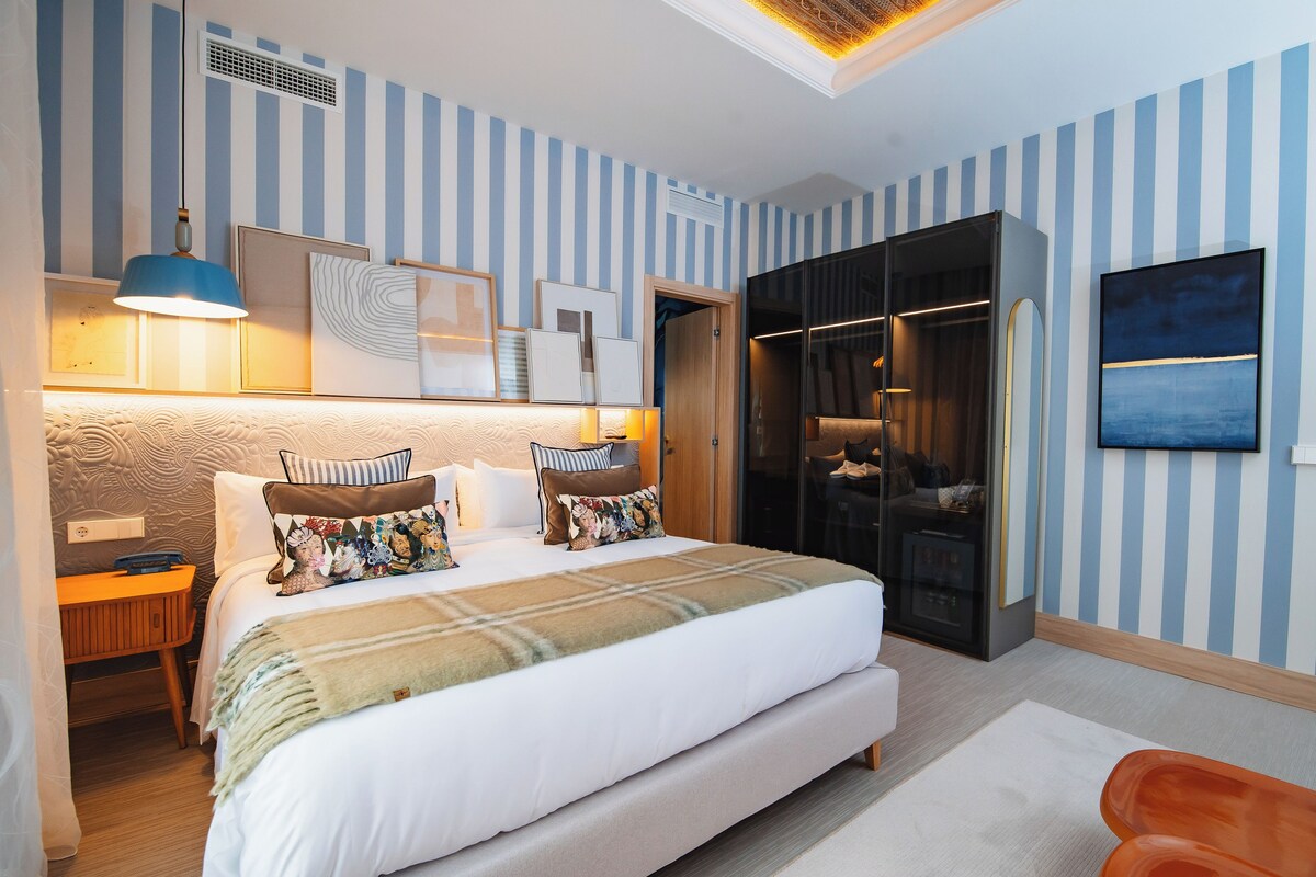 A hotel room with a large bed, a wardrobe, a desk, and a TV on the wall.