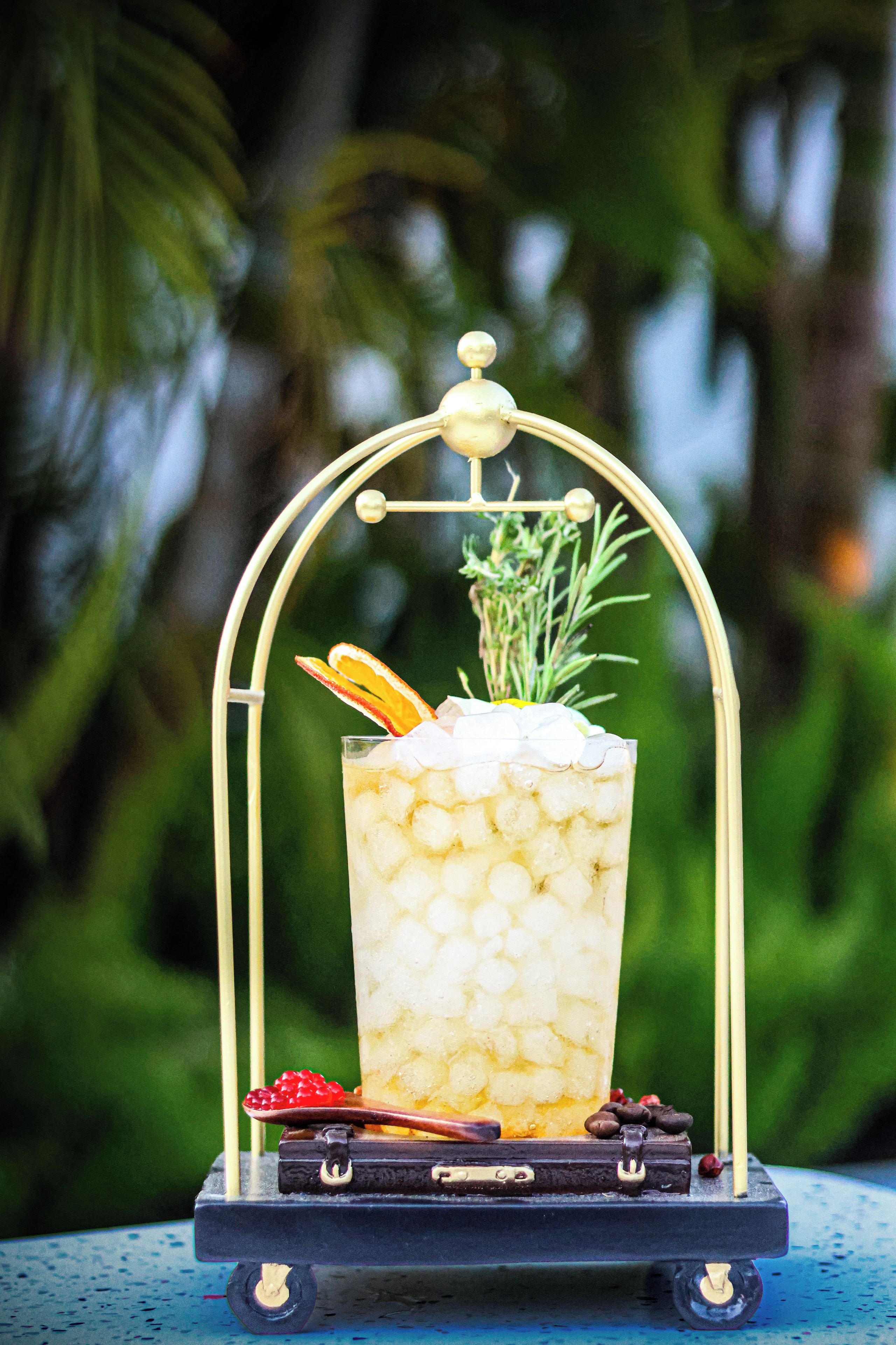 A tall glass of iced beverage with a garnish, placed on a cart with a metal frame.