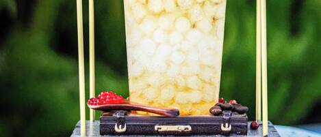 A tall glass of iced beverage with a garnish, placed on a cart with a metal frame.