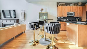 Una cocina moderna con armarios de madera, microondas integrado y un comedor con un taburete de bar tapizado en negro y una mesa redonda.
