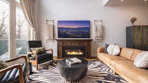 Una sala de estar moderna con chimenea, un cuadro grande de un paisaje urbano y vistas al exterior.