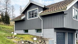 Une maison à deux étages, avec une façade grise, un toit en tuiles et des fondations en pierre.