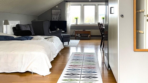 Une chambre à coucher avec un lit, une chaise, une télévision et une fenêtre avec des rideaux.