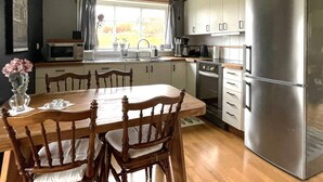 Une cuisine équipée d’une table à manger, de chaises, d’un réfrigérateur, d’un évier et d’une fenêtre avec des rideaux.