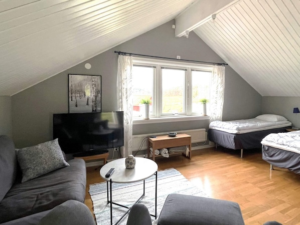 A cozy attic bedroom with a TV, two beds, a sofa, and a small table.