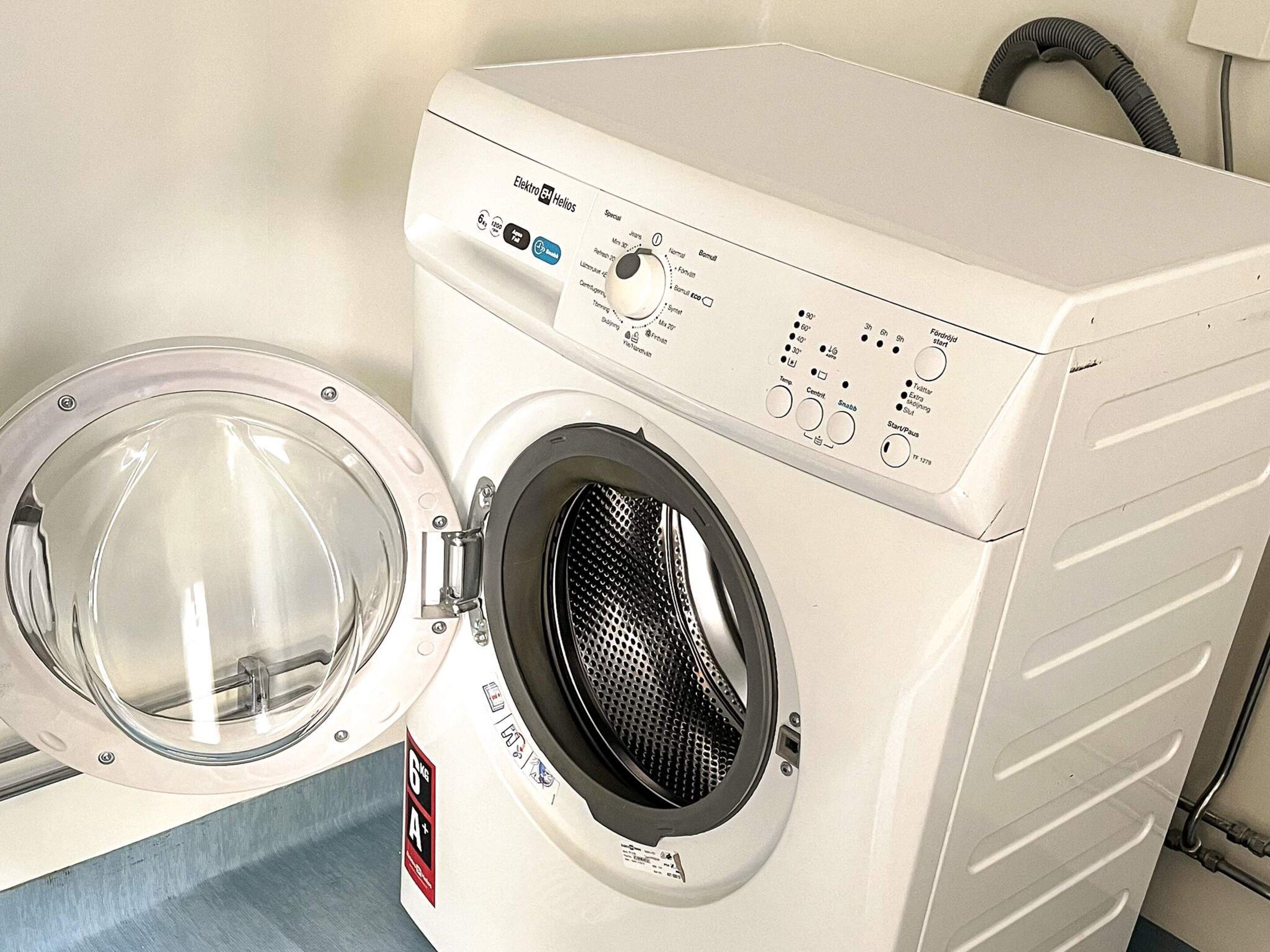 A front-loading washing machine with a control panel, a transparent door, and a hose.