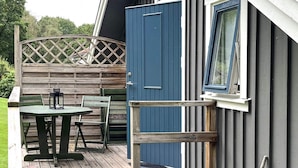 Une terrasse en bois avec une table et des chaises, une porte bleue et une fenêtre.