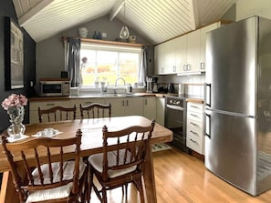 Una cocina con armarios de madera, un refrigerador de acero inoxidable, una mesa de comedor con sillas y una ventana con cortinas.