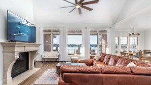 A spacious living room with a fireplace, leather sofa, and a television displaying an underwater scene. - Lakefront Family Retreat with Game Room Fun (Sanford)