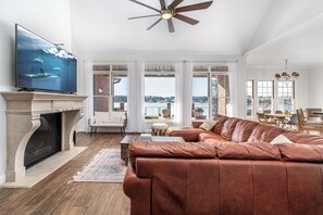 A spacious living room with a fireplace, leather sofa, and a television displaying an underwater scene. - Lakefront Family Retreat with Game Room Fun (Sanford)