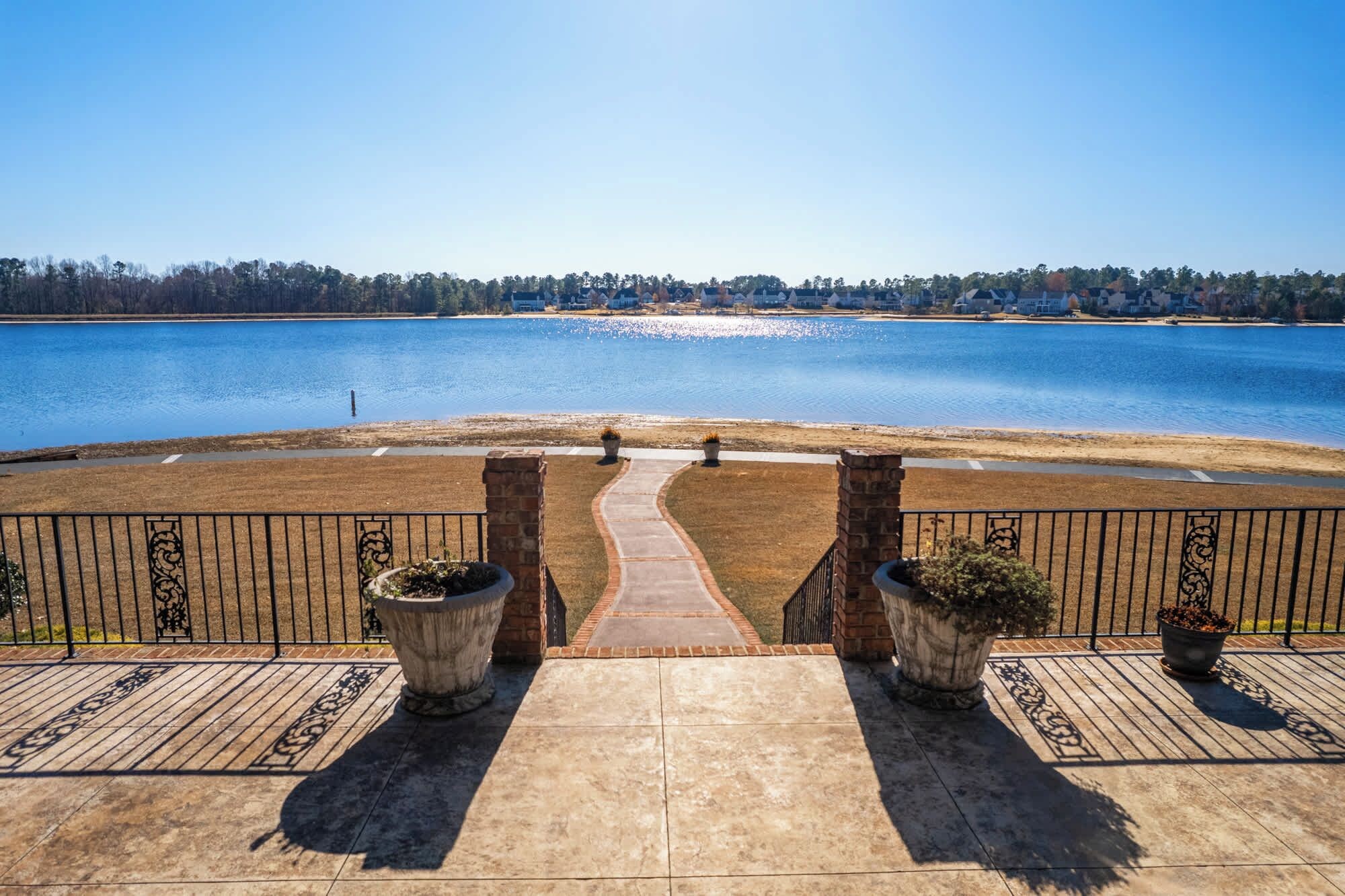A patio with a view of a lake, a paved walkway, and two planters.