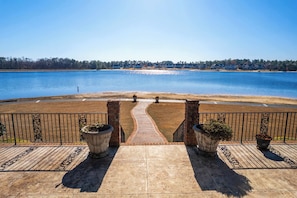 Enjoy a serene lakeside view from this outdoor space, surrounded by lush greenery and a distant residential area.
