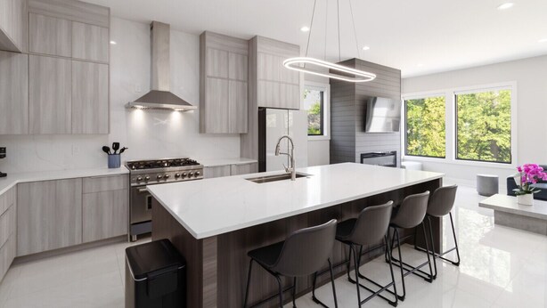 A modern kitchen with a central island, bar stools, and a large window providing a view of greenery. - Brand-New 3Story Home with Rooftop in Midtown (Atlanta)