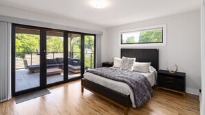 A modern bedroom with a large bed, a nightstand, a dresser, and a sliding glass door leading to an outdoor area. - Brand-New 3Story Home with Rooftop in Midtown (Atlanta)