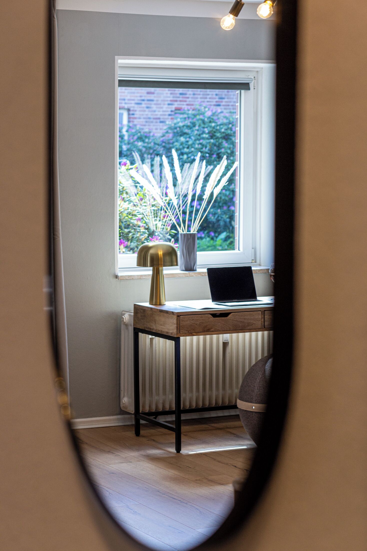 A room with a desk, a laptop, a radiator, and a window with a view of greenery.