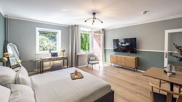 A modern bedroom with a large bed, a desk, a chair, a TV, and a dining table. - have-a-nice-stay - modern, near train station, quiet, 15 minutes by train to HH (Ahrensburg)