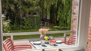 A balcony with a table set for two, a vase with flowers, and a view of a garden and parked bicycles. - have-a-nice-stay - modern, near train station, quiet, 15 minutes by train to HH (Ahrensburg)