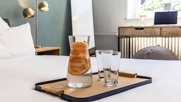 A bed with a tray holding a glass of water with lemon slices, two clear glasses, and a wooden tray.