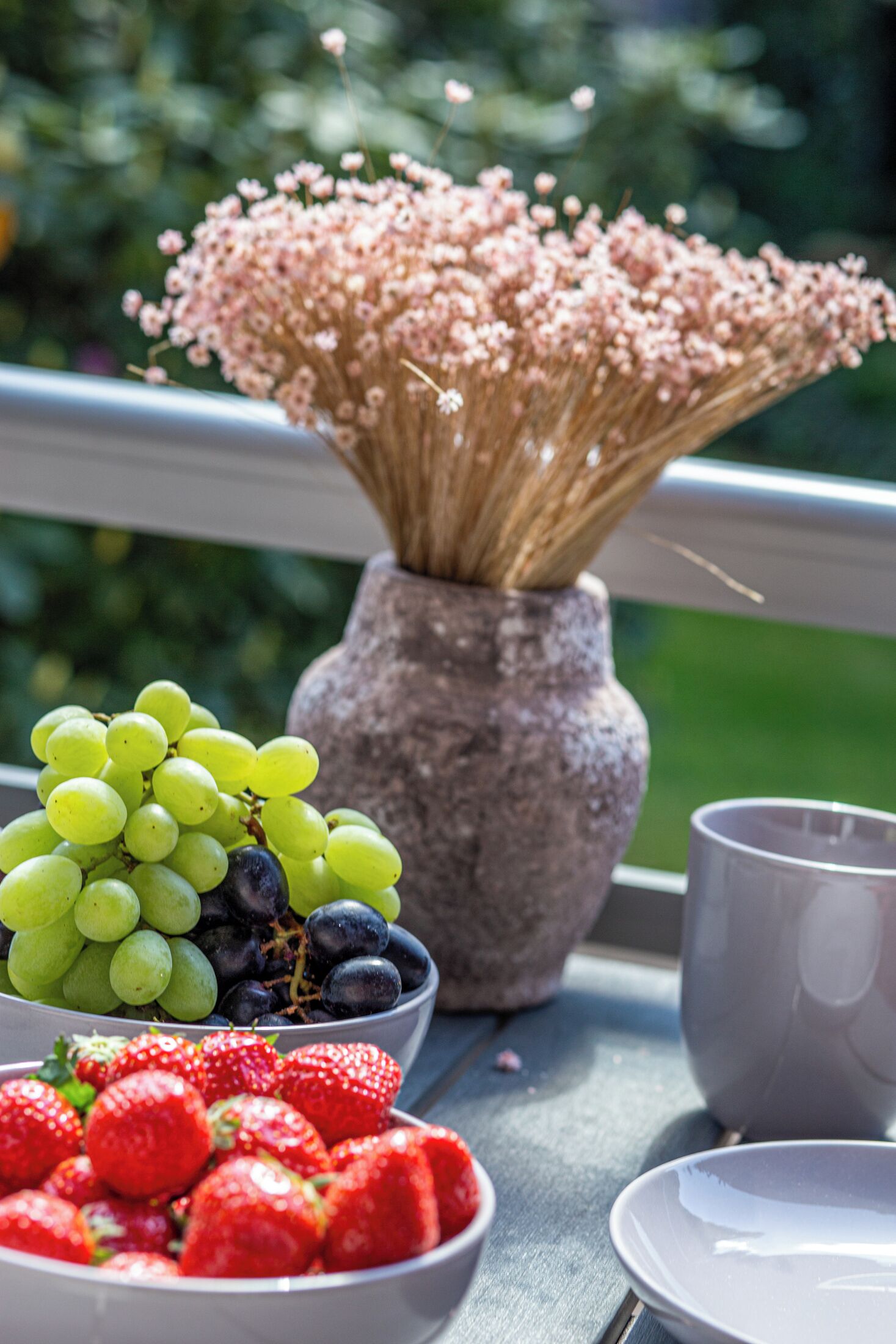 Uma mesa com uma tigela de uvas, uma tigela de morangos e um vaso com flores.