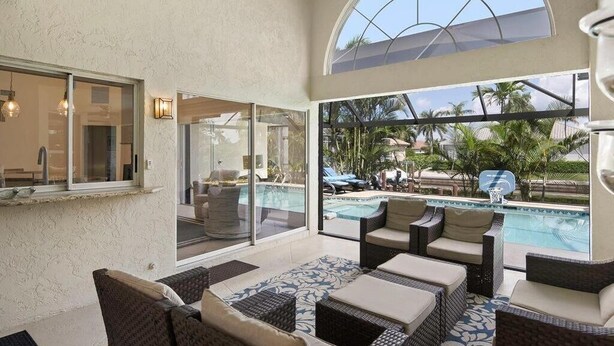 A spacious indoor area with a pool view, wicker furniture, and a ceiling fan. - Waterfront 3BR retreat with heated pool, WiFi, and room for 8. (Marco Island)