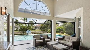 A spacious indoor area with a large window overlooking a swimming pool, furnished with wicker sofas and a patterned rug. - Waterfront 3BR retreat with heated pool, WiFi, and room for 8. (Marco Island)