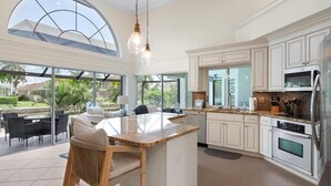 A spacious kitchen with white cabinetry, a large island, and a dining area with outdoor seating. - Waterfront 3BR retreat with heated pool, WiFi, and room for 8. (Marco Island)