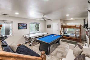 A pool table, a sofa, a bunk bed, and a ceiling fan in a room with windows and artwork on the walls.