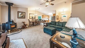 A living room with a fireplace, a sofa, a dining table with chairs, and a ceiling fan. - Eagle Retreat ~ Mountain Escape • New • With AC (Shaver Lake)