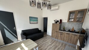 A compact living space with a kitchenette, a black sofa, a dining table with chairs, and a painting on the wall. - Amiens, l'appartement douillet 2-4P (Amiens)
