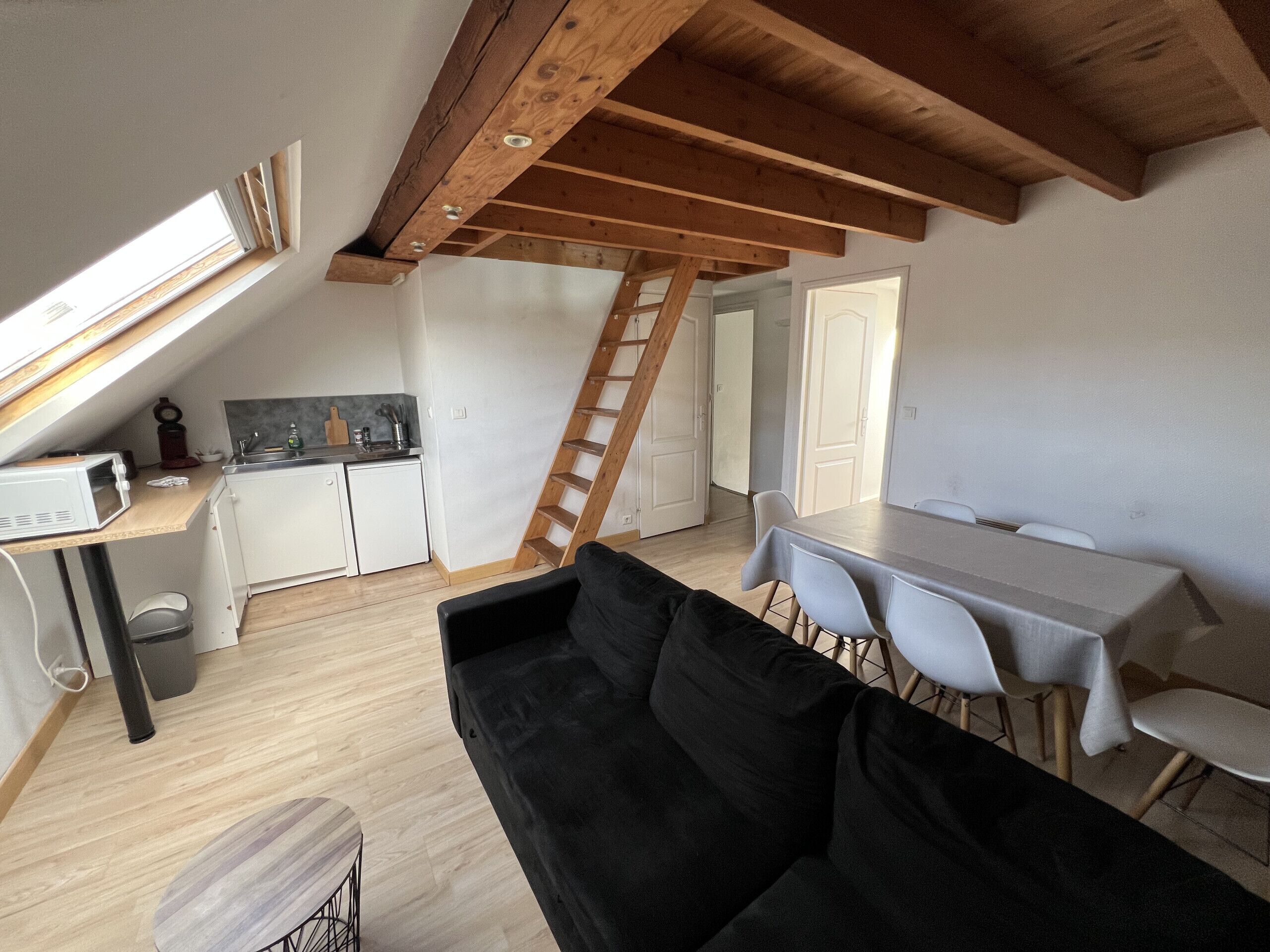A compact living space with a loft bedroom, a kitchenette, a dining area, and a black sofa.