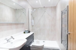 A modern bathroom with a large sink, mirror, and shower. - Hideaway Cottages - Greenacres Estates (Tenby)