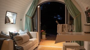 A cozy interior with a sofa, a small table, and a view of the outdoors through a doorway. - Hideaway Cottages - Greenacres Estates (Tenby)