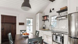 Une cuisine moderne avec des meubles blancs, un réfrigérateur en acier inoxydable, un four encastré et un coin repas comprenant une table et des chaises en bois.
