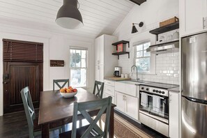 A modern kitchen with white cabinetry, a stainless steel refrigerator, a built-in oven, and a dining area with a wooden table and chairs. - Ready Aim (Atlanta)
