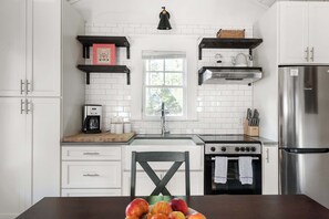 Una cocina moderna con armarios blancos, un refrigerador de acero inoxidable, una estufa a gas y una ventana con vistas a zonas verdes.